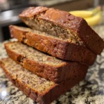 Delicious loaf of almond flour banana bread sliced on a wooden board, surrounded by almonds, banana, and flour.